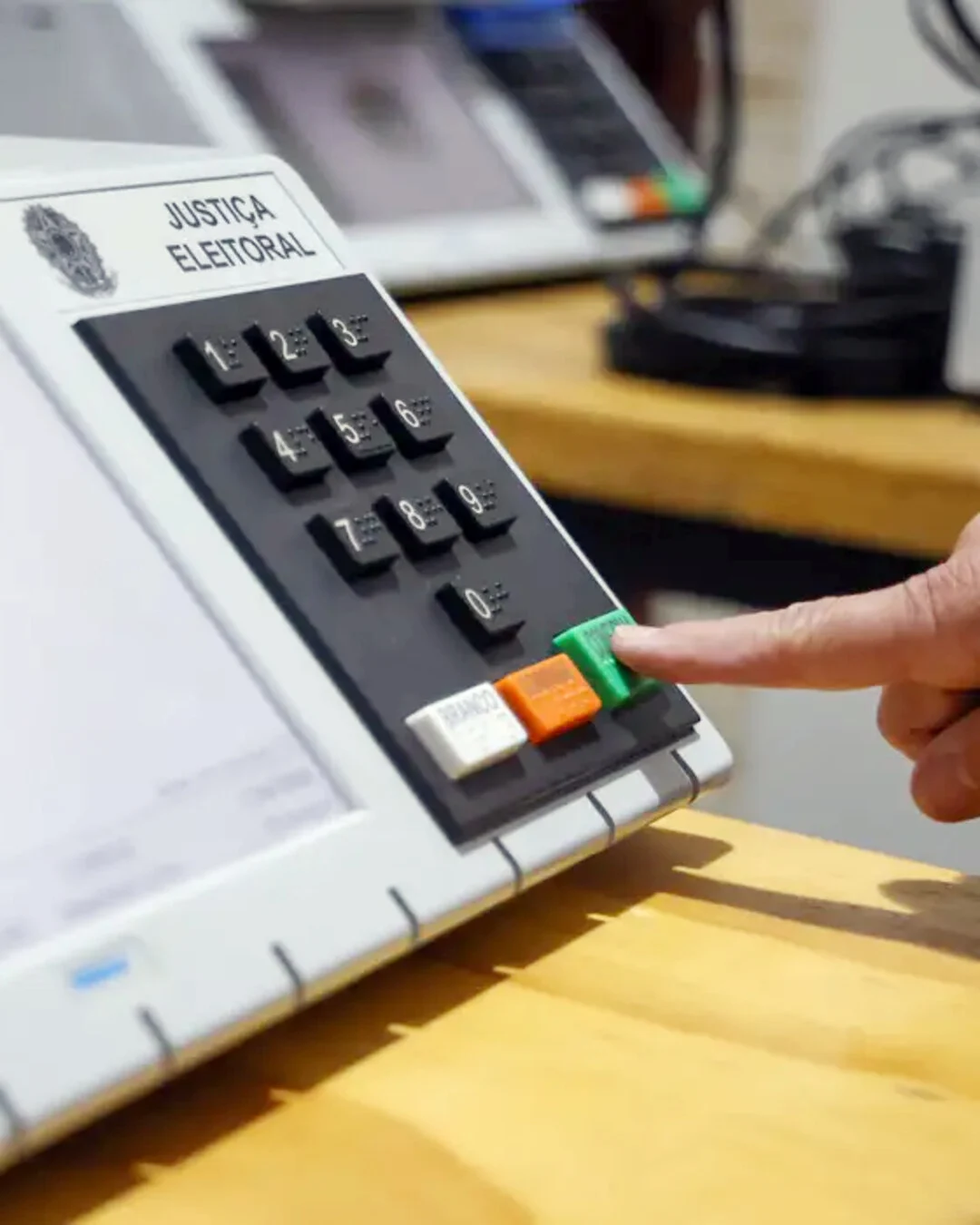 Teclado de urna eletrônica, com um dedo pressionando o botão verde de confirmação.