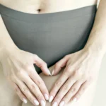 Mãos formam um coração sobre o ventre de uma mulher.