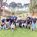 Grupo de ex-combatentes posa para foto em um gramado, com araucárias ao fundo.