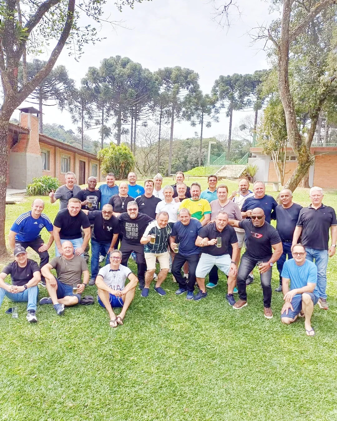 Grupo de ex-combatentes posa para foto em um gramado, com araucárias ao fundo.