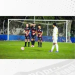 Três jogadores formam a barreira diante do gol enquanto outro se prepara para cobrar a falta.